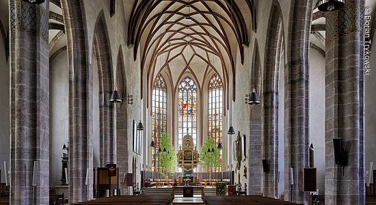 Großes Kirchenschiff mit Säulen und Bänken, am Ende ein hell erleuchtetes, prunkvolles Seitenschiff