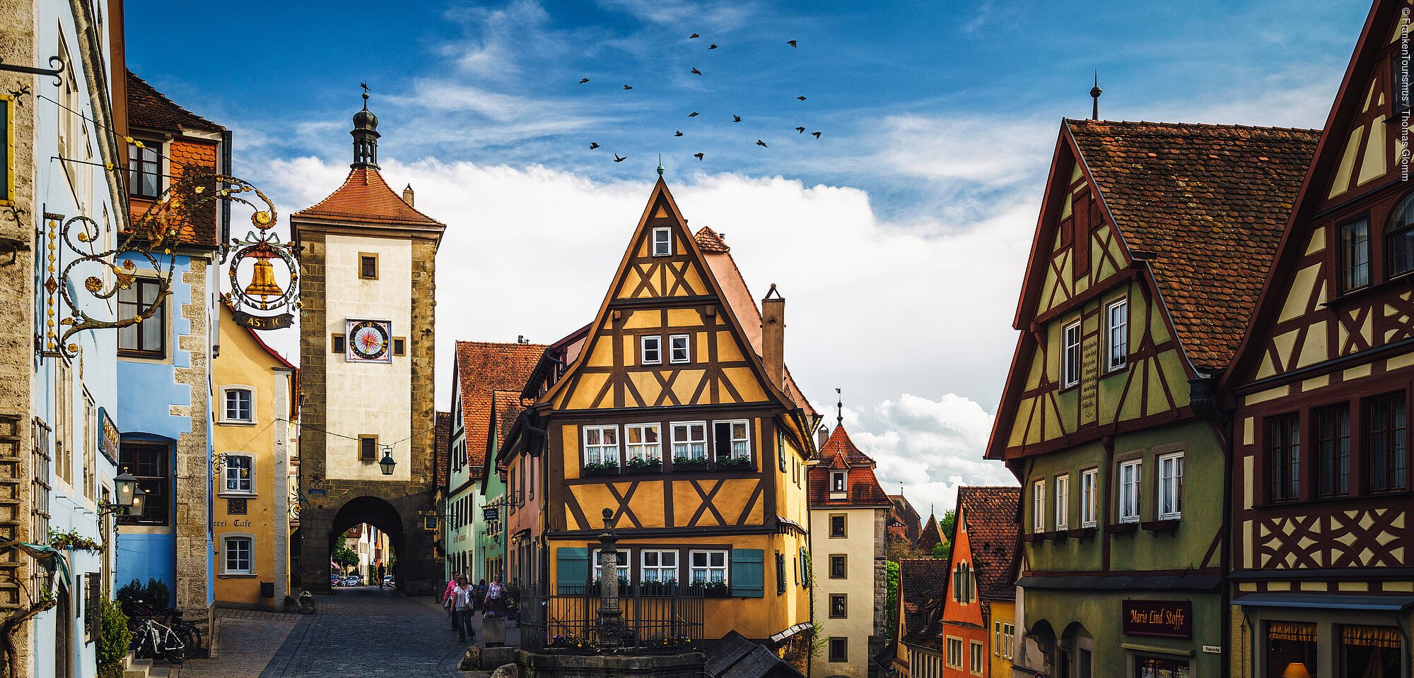 Straßengabelung in einer mittelalterlichen Altstadt mit bunten Fachwerkhäusern und Torturm
