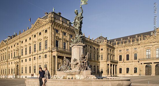 Eine steinerne Statue im Sonnenschein vor einem barocken Prachtbau