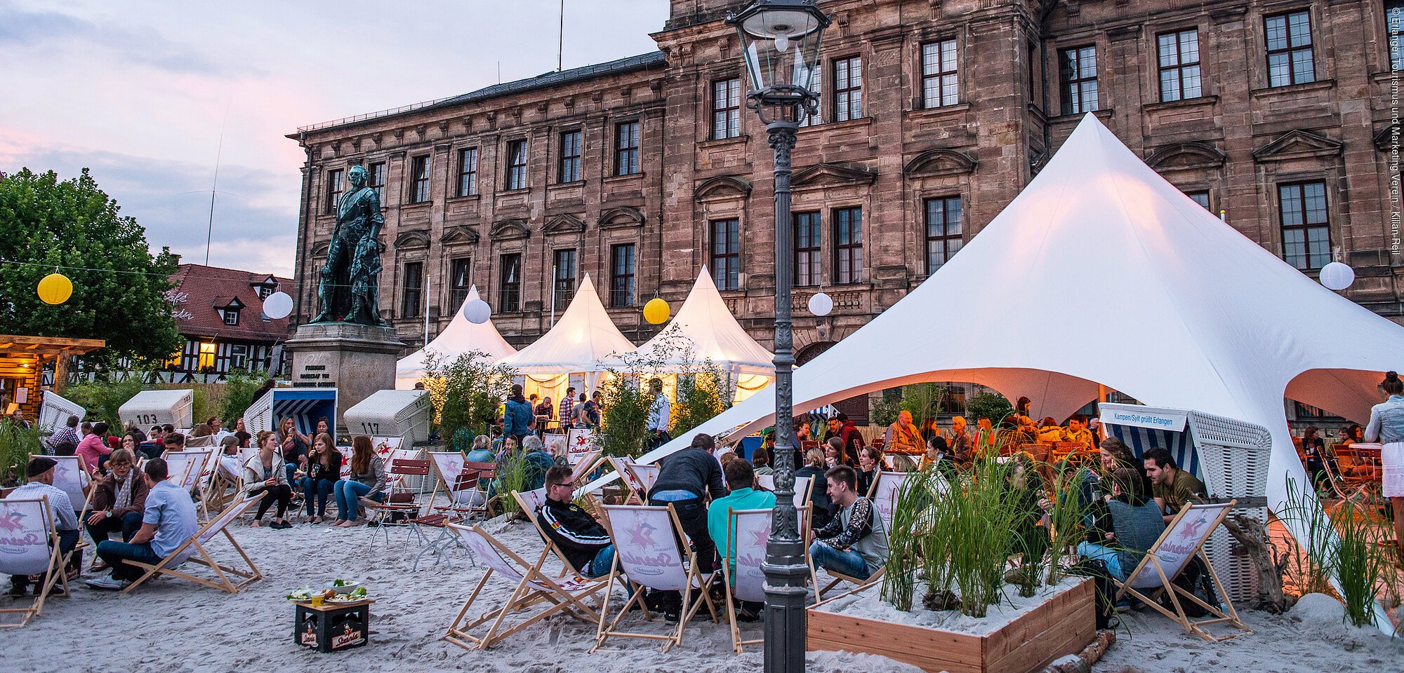 Vor einem historischen Gebäude ist ein Zelt mit Getränken und Strandflair aufgebaut