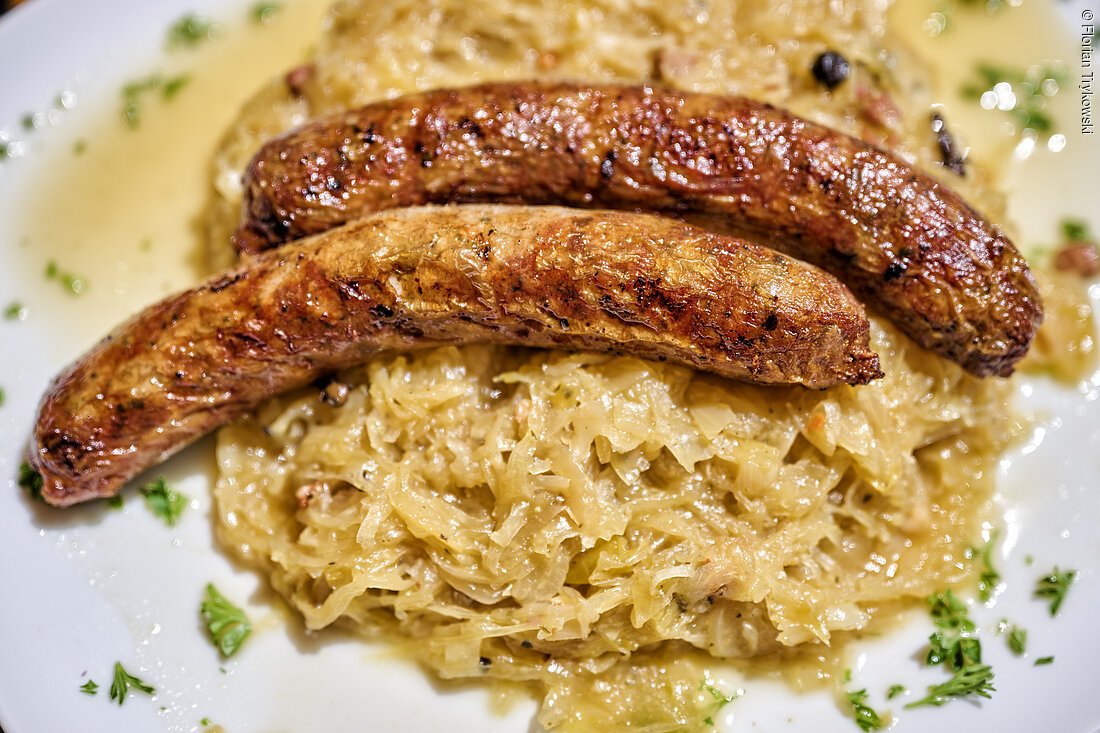 Zwei gebratene Würste auf einem Bett aus Sauerkraut, garniert mit Petersilie auf einem weißen Teller.