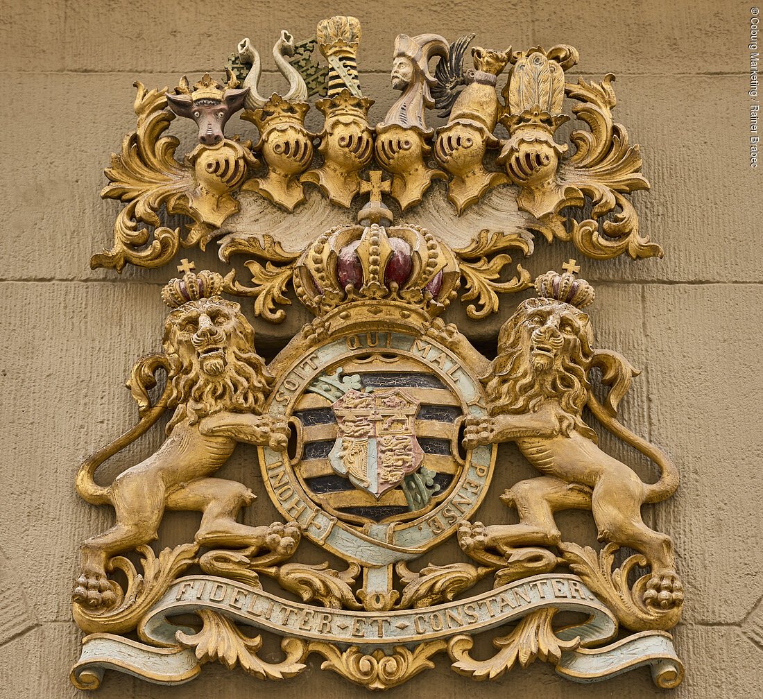 Ein kunstvoll gestaltetes Wappen mit zwei Löwen, die ein Schild halten, verziert mit Kronen und dekorativen Elementen.