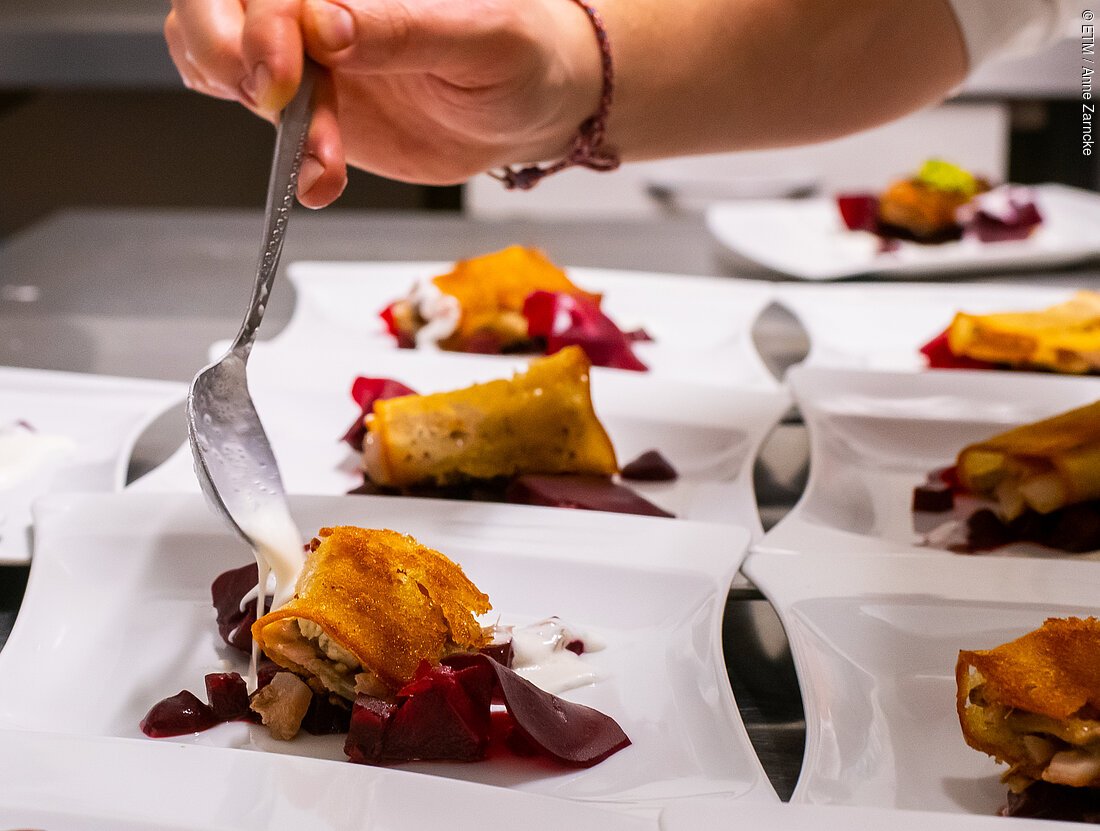 Eine Person richtet mehrere Teller mit einer Vorspeise.